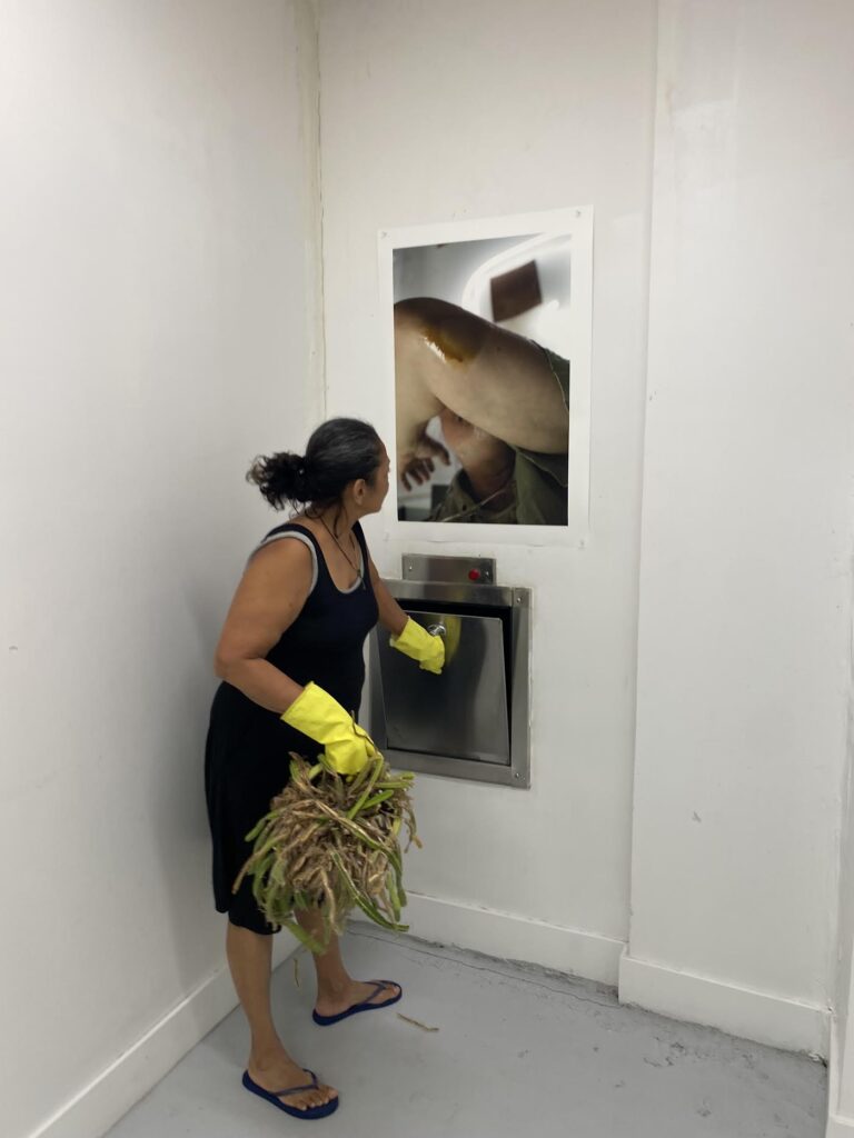 A resident throws out trash beneath Markus Haugg’s “Prefer Not To See,” August 2025. (Photo by Alfredo Travieso, courtesy of Trashroom Gallery).