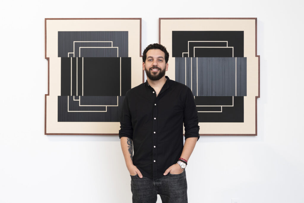 Guillermo Garcia Cruz sin front of two of his enigmatic “glitch” pieces. (Photo by Karli Evans, courtesy of Fountainhead Arts).